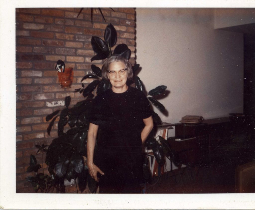 An older woman standing in front of a brick wall smiling at the camera.