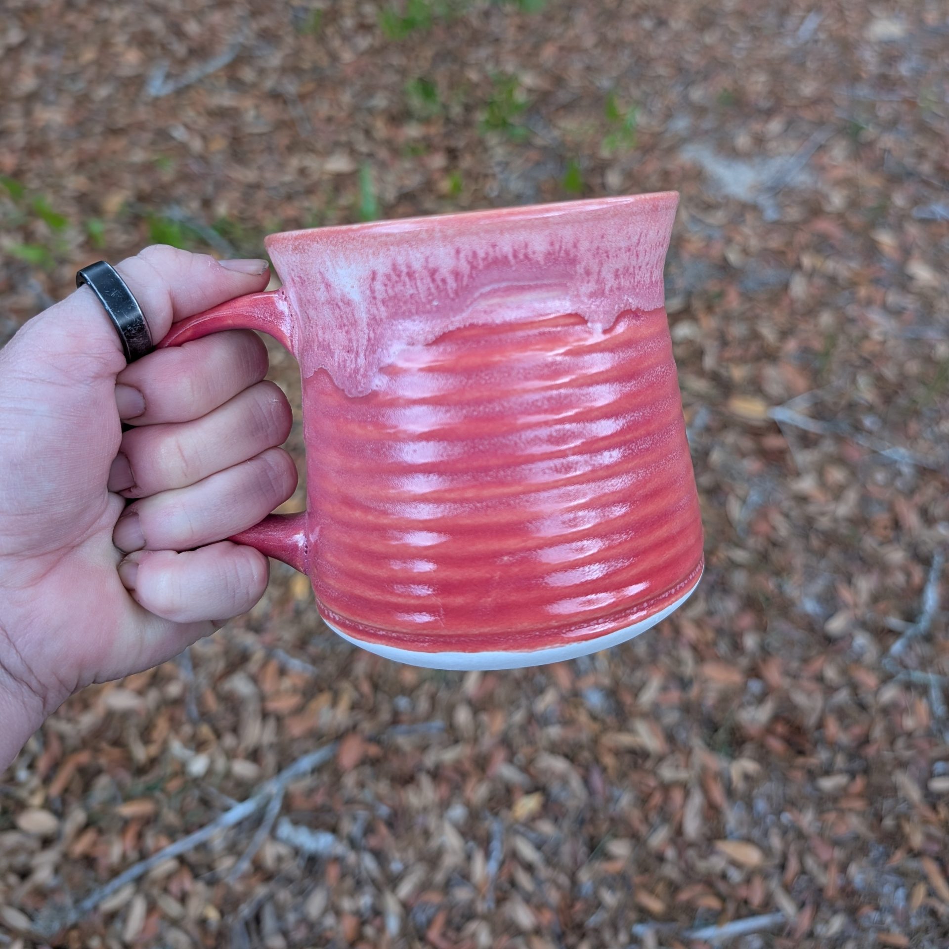 A hand holding a pink ceramic mug, with a natural background.