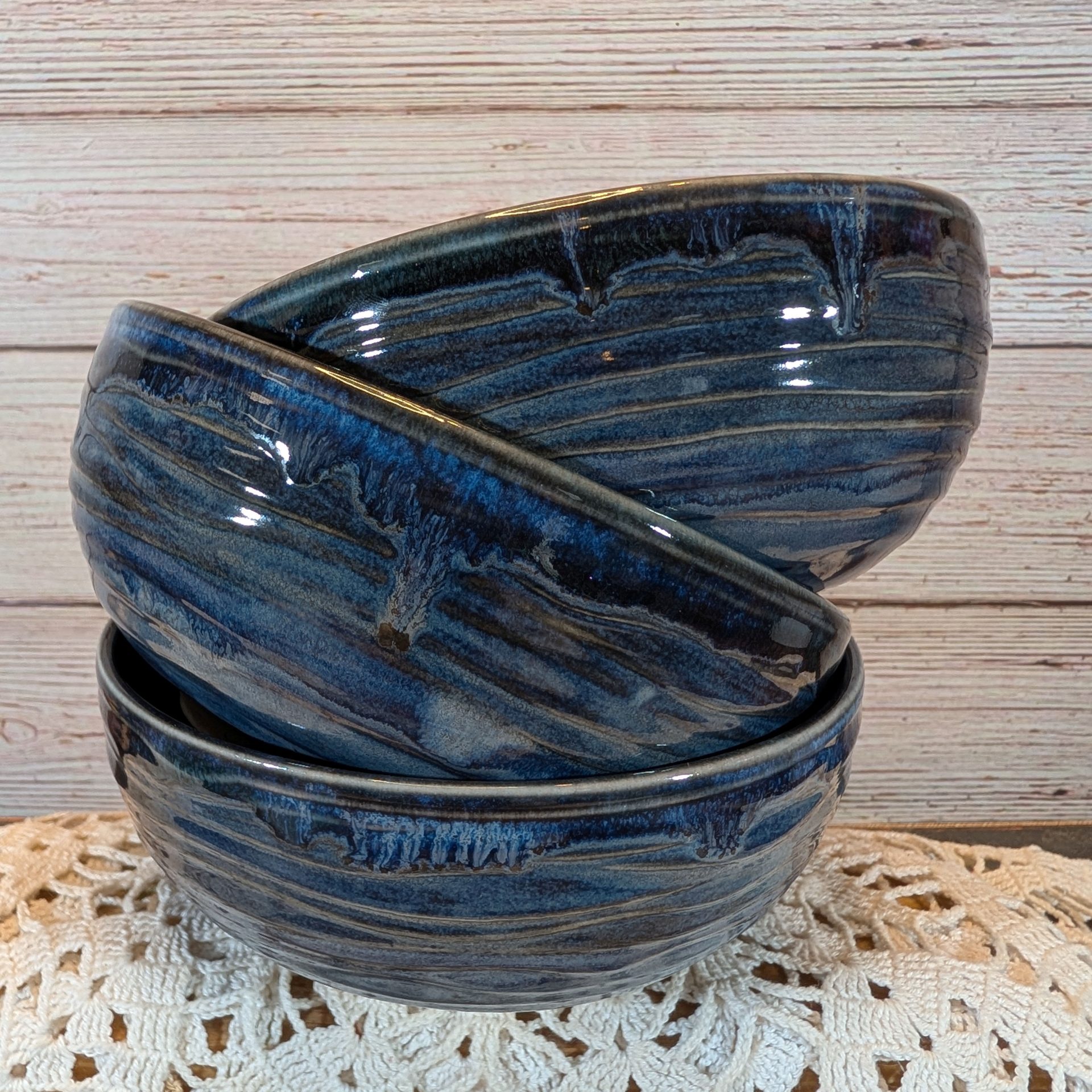 Three blue bowls, stacked on top of each other, on a lace doily and a wooden background.
