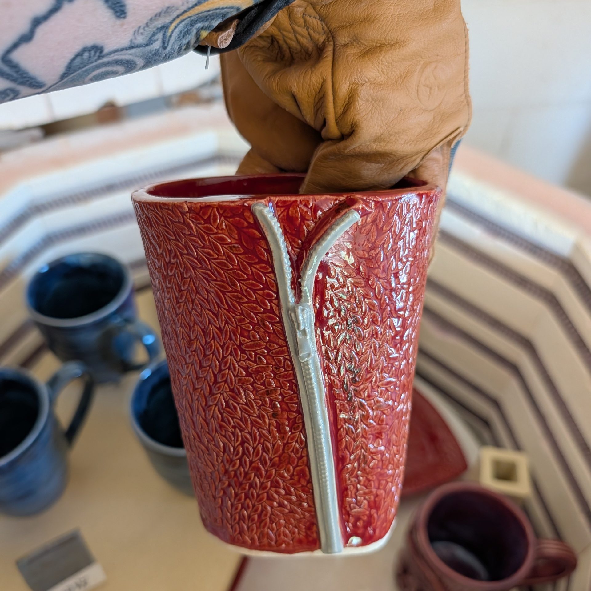 A gloved hand holding a still-warm vase having just pulled it out of the kiln.